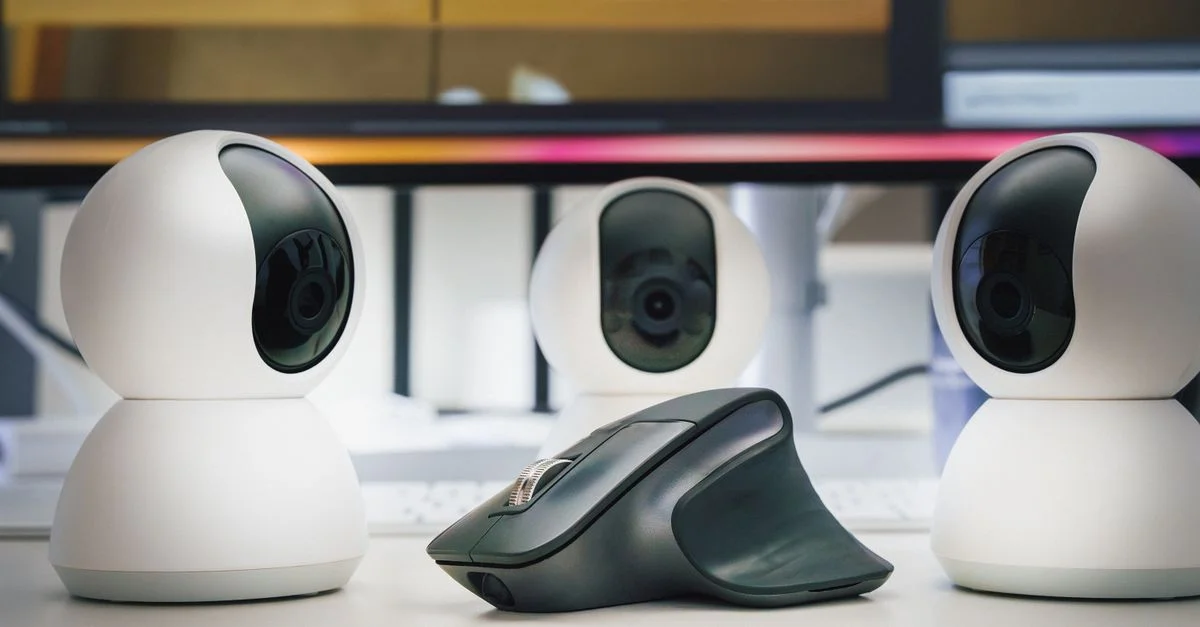 Trois webcams blanches et une souris d'ordinateur sur un bureau, mettant en avant la technologie moderne de bureau.