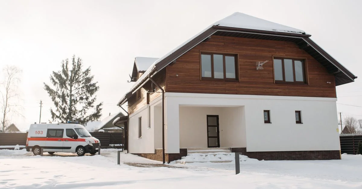 Une maison suburbane avec un paysage enneigé et une ambulance garée à proximité.